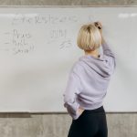 Female writing workout schedule on whiteboard in gym setting.