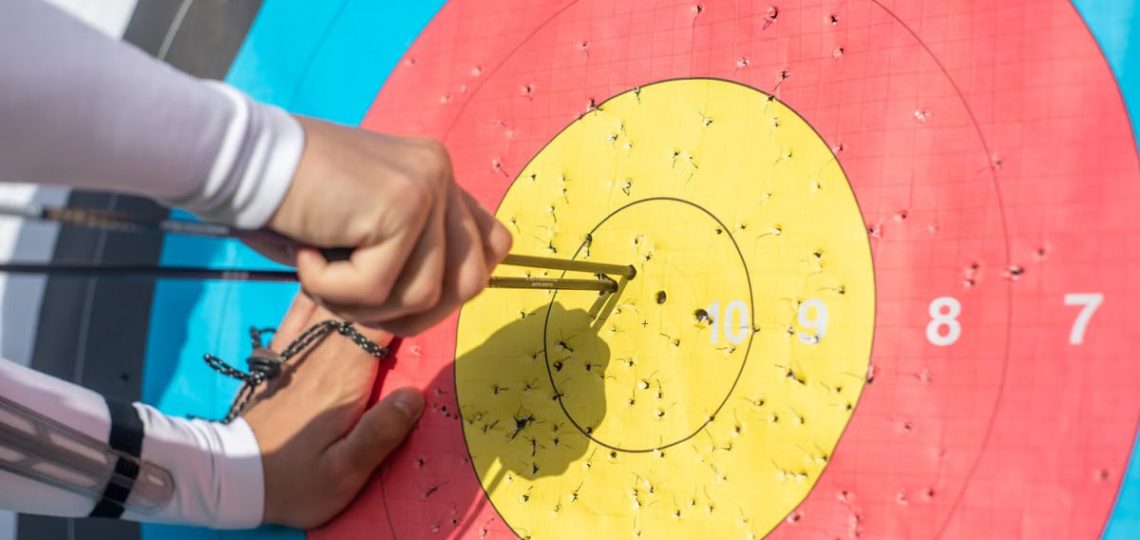 An archer retrieves arrows from a colorful archery target during a sunny day outdoors.
