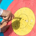 An archer retrieves arrows from a colorful archery target during a sunny day outdoors.