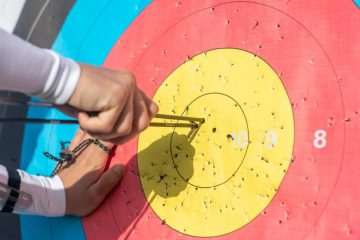 An archer retrieves arrows from a colorful archery target during a sunny day outdoors.